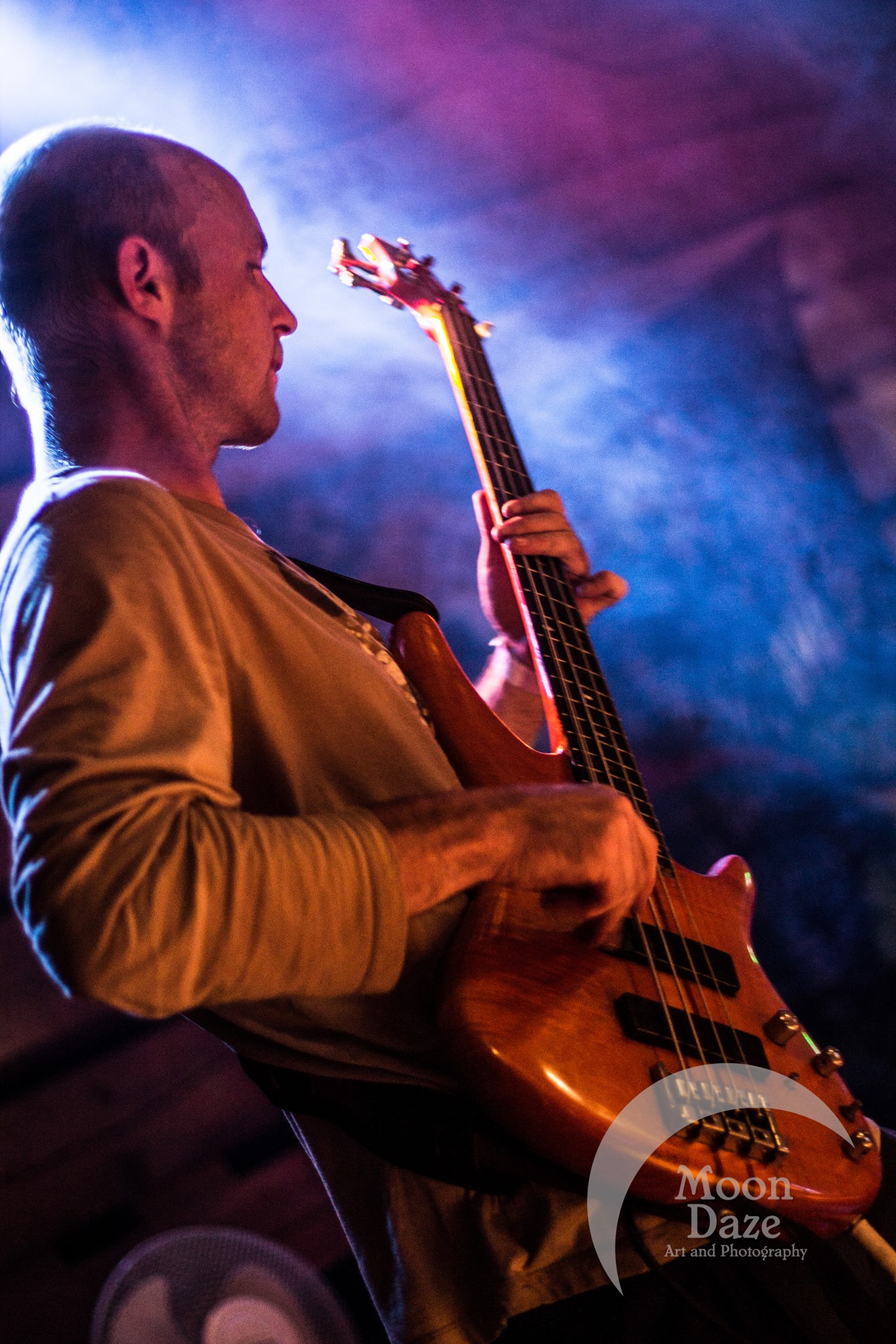 A photo of Greg Goad playing bass live on stage under purple concert lighting and fog. Taken by Moon Daze photography.